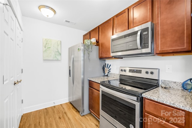 kitchen with appliances with stainless steel finishes, light wood-type flooring, brown cabinetry, and visible vents