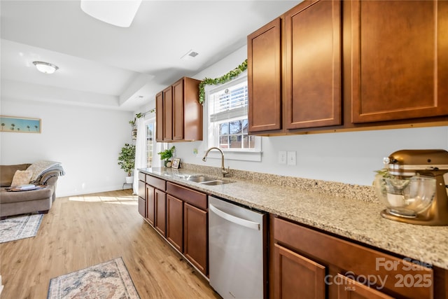 kitchen with a sink, light wood-style floors, stainless steel dishwasher, light stone countertops, and a tray ceiling