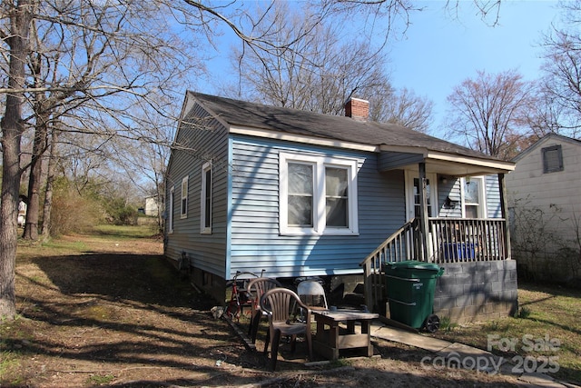 view of front of home featuring a porch, a chimney, and a shingled roof