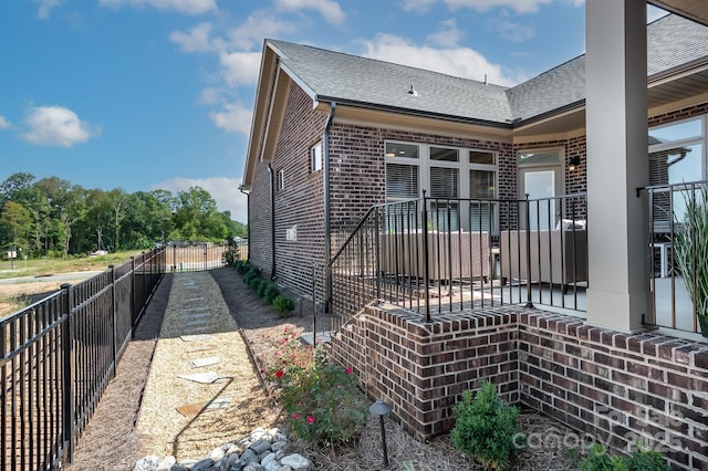 view of home's exterior featuring brick siding, a shingled roof, and fence