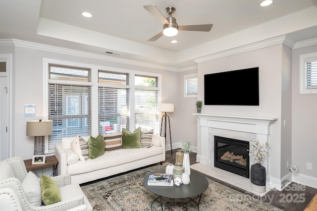 living room with baseboards, visible vents, a raised ceiling, ornamental molding, and a fireplace