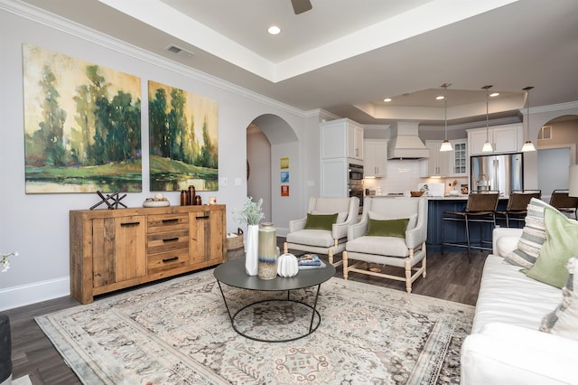 living area featuring a tray ceiling, dark wood-style flooring, arched walkways, visible vents, and baseboards