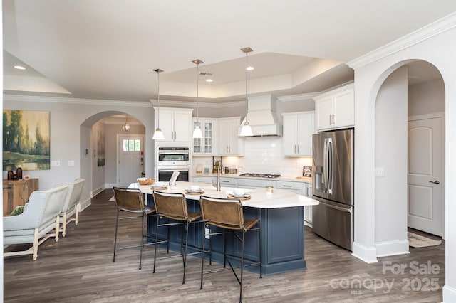 kitchen featuring arched walkways, decorative backsplash, a raised ceiling, custom range hood, and stainless steel appliances