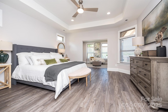 bedroom featuring ceiling fan, recessed lighting, wood finished floors, baseboards, and a tray ceiling