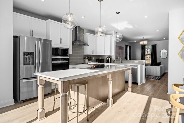 kitchen with a center island, appliances with stainless steel finishes, a sink, a peninsula, and wall chimney exhaust hood