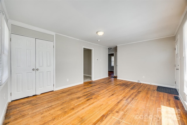 unfurnished bedroom featuring light wood-style flooring, a closet, ornamental molding, and baseboards