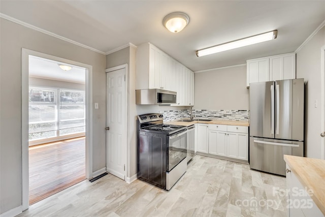 kitchen with appliances with stainless steel finishes, butcher block countertops, ornamental molding, and white cabinetry