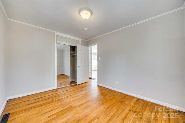 unfurnished bedroom featuring a closet, baseboards, crown molding, and light wood finished floors