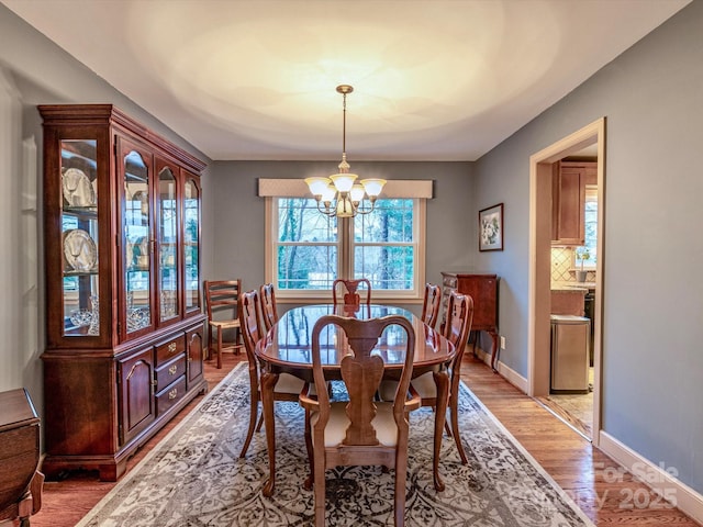 dining space featuring an inviting chandelier, light wood-style flooring, and baseboards