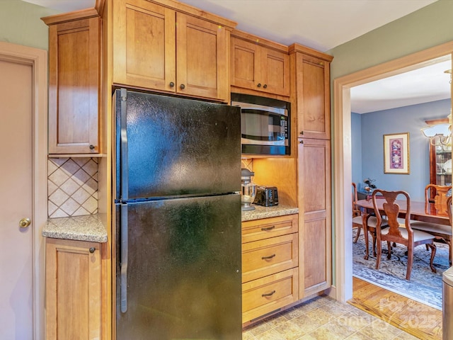 kitchen featuring brown cabinets, decorative backsplash, freestanding refrigerator, light stone countertops, and built in microwave