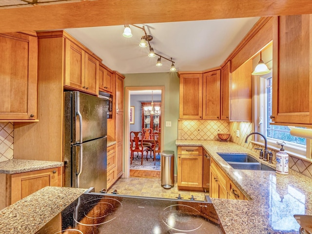 kitchen featuring brown cabinets, backsplash, freestanding refrigerator, a sink, and light stone countertops