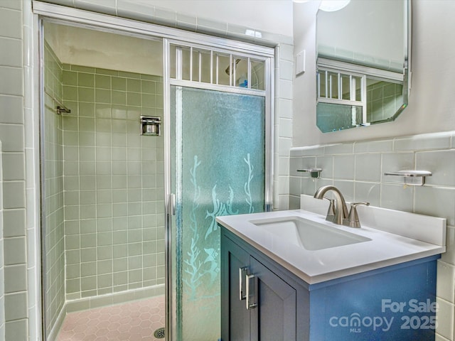 bathroom featuring tile walls, wainscoting, a shower stall, and vanity