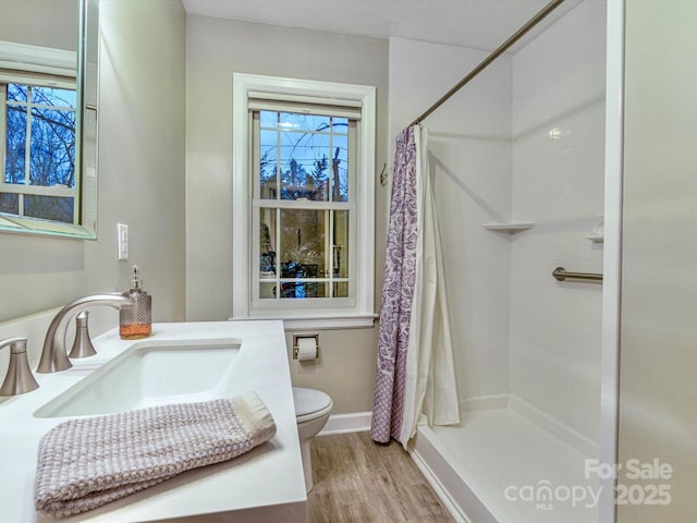 bathroom featuring baseboards, tiled shower, toilet, wood finished floors, and vanity