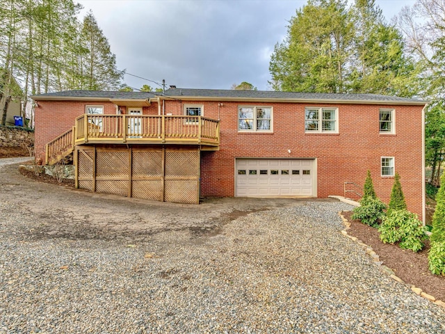 view of front of home featuring a deck, an attached garage, brick siding, stairway, and gravel driveway