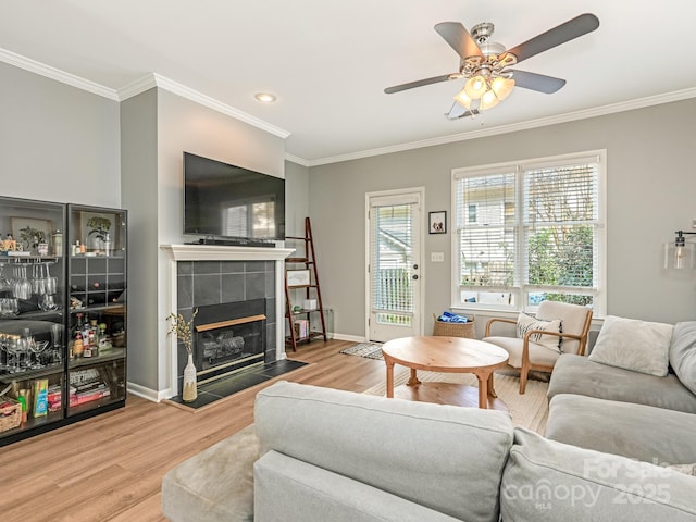 living room featuring baseboards, a tile fireplace, ceiling fan, ornamental molding, and wood finished floors