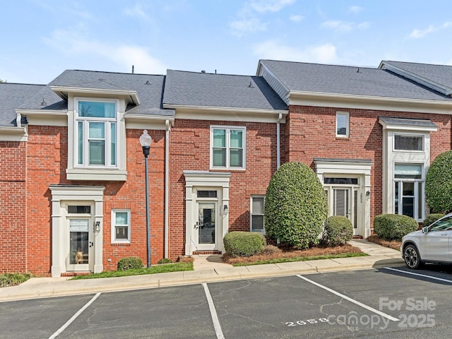 exterior space featuring uncovered parking, brick siding, and a shingled roof