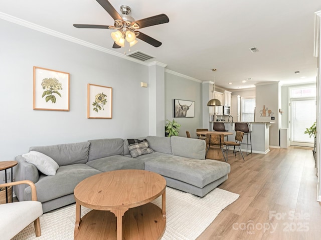 living area with light wood-style floors, ceiling fan, visible vents, and ornamental molding