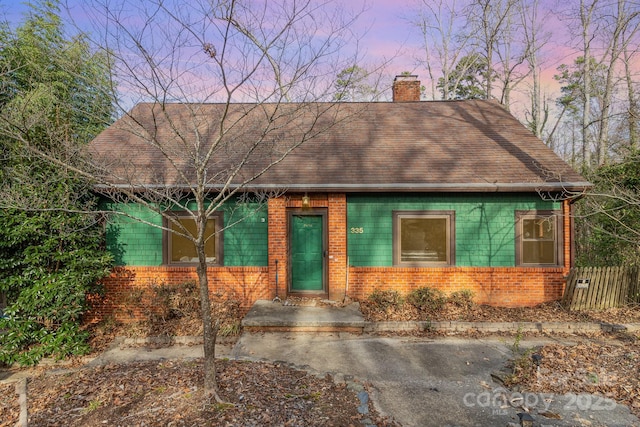 view of front of house with brick siding, a chimney, and roof with shingles