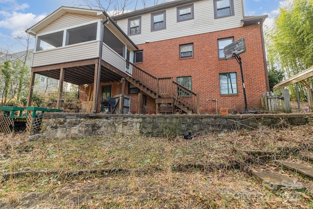 back of property featuring a sunroom, brick siding, and stairs