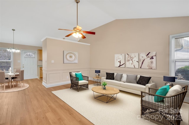 living area with lofted ceiling, a decorative wall, ceiling fan with notable chandelier, light wood-style floors, and wainscoting