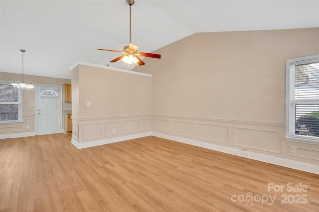 spare room featuring lofted ceiling, light wood-style flooring, and ceiling fan with notable chandelier