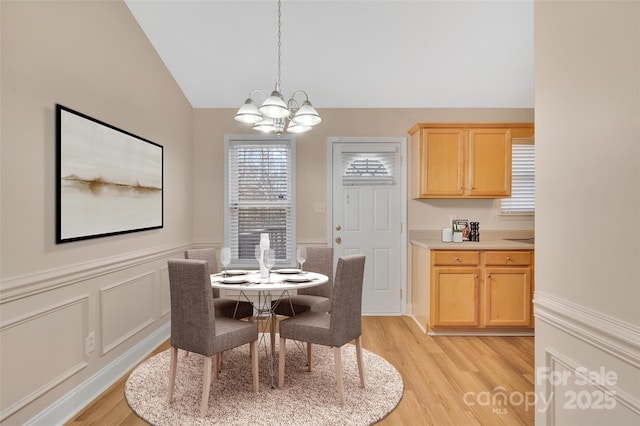 dining space with lofted ceiling, light wood-style floors, a wainscoted wall, and an inviting chandelier