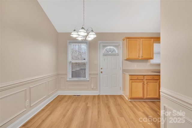 unfurnished dining area featuring a notable chandelier, visible vents, wainscoting, vaulted ceiling, and light wood-type flooring