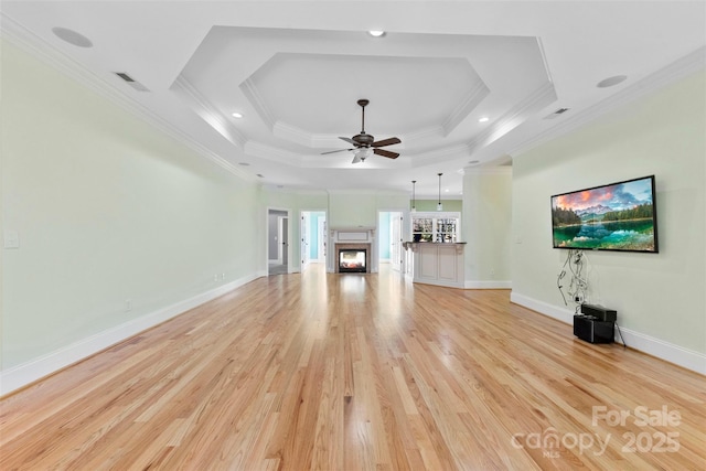 unfurnished living room with ceiling fan, light wood-style floors, a lit fireplace, ornamental molding, and a tray ceiling