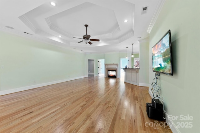 unfurnished living room featuring ceiling fan, a lit fireplace, a raised ceiling, and visible vents