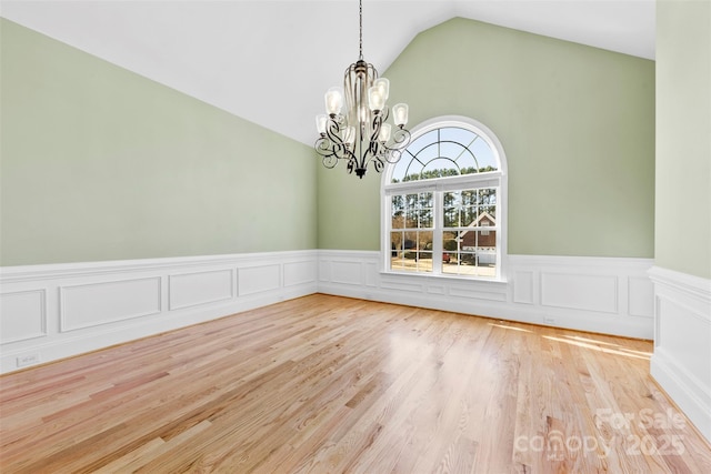 unfurnished dining area with lofted ceiling, a wainscoted wall, wood finished floors, and a notable chandelier