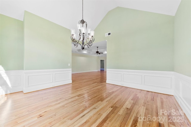 spare room featuring a wainscoted wall, lofted ceiling, visible vents, light wood-style floors, and ceiling fan with notable chandelier