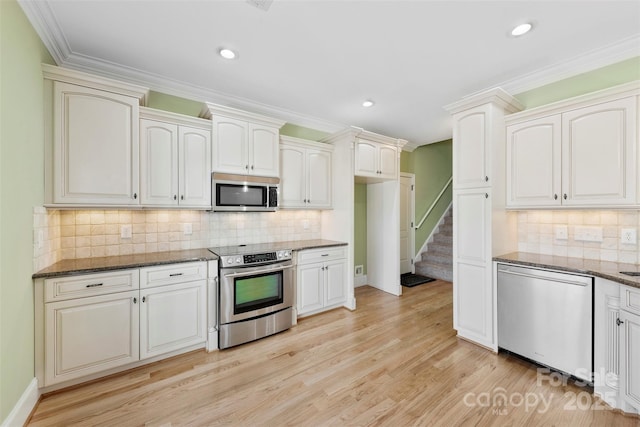 kitchen featuring light wood-style flooring, ornamental molding, dark stone countertops, stainless steel appliances, and backsplash