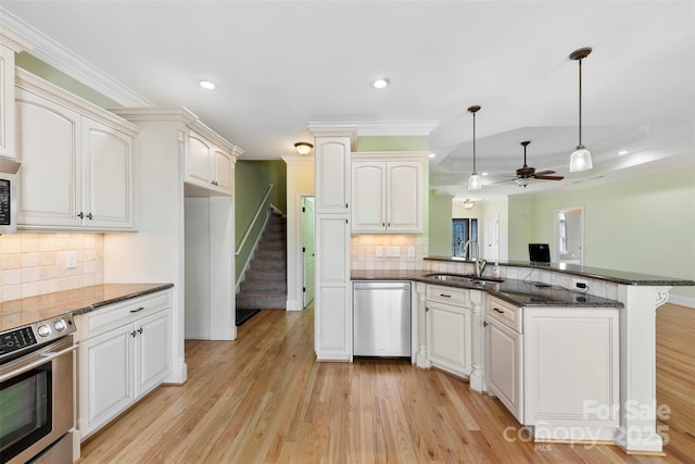 kitchen with stainless steel appliances, a peninsula, a sink, light wood-style floors, and crown molding