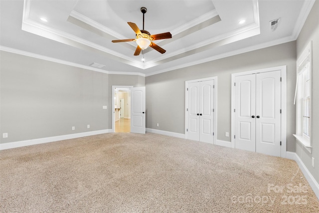 unfurnished bedroom featuring two closets, a raised ceiling, light colored carpet, ornamental molding, and baseboards