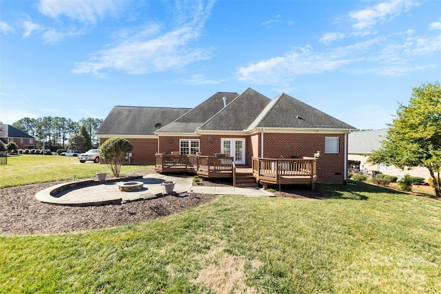 back of property featuring an outdoor fire pit, a wooden deck, a shingled roof, a yard, and brick siding