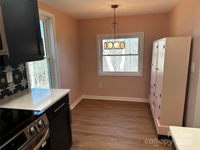 kitchen featuring wood finished floors, baseboards, light countertops, dark cabinetry, and stainless steel range with electric stovetop