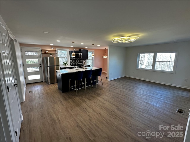 kitchen featuring stainless steel appliances, dark wood-type flooring, a breakfast bar area, and a healthy amount of sunlight