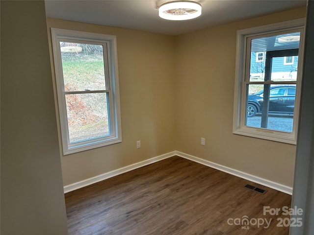 spare room featuring dark wood-style floors, visible vents, and baseboards