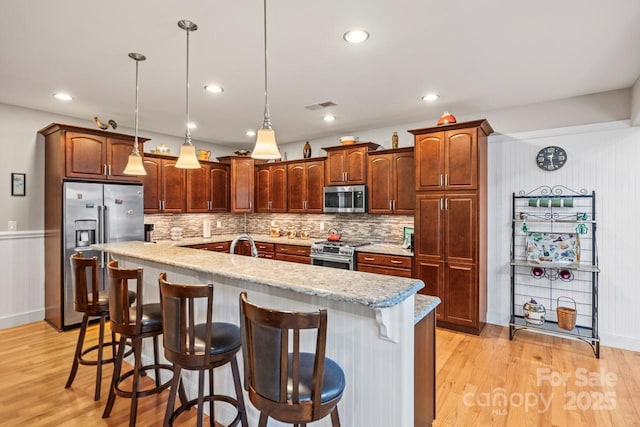 kitchen with tasteful backsplash, premium appliances, a kitchen island with sink, light wood-style floors, and a sink