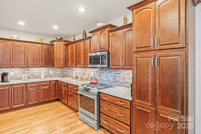 kitchen with recessed lighting, appliances with stainless steel finishes, light stone countertops, light wood finished floors, and tasteful backsplash