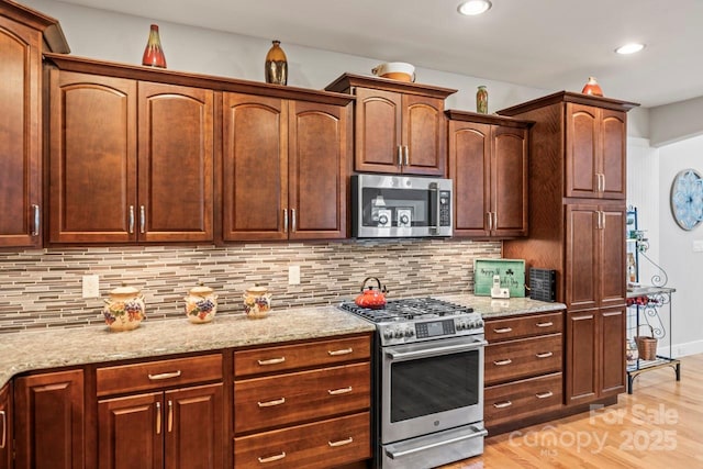 kitchen featuring appliances with stainless steel finishes, light stone countertops, light wood-type flooring, backsplash, and recessed lighting