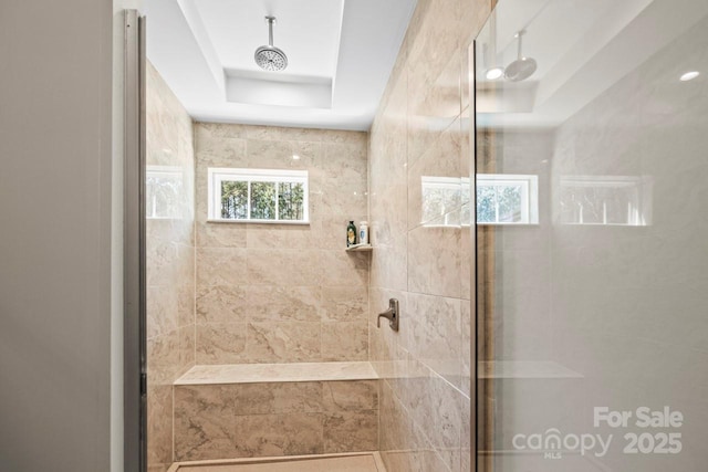 bathroom with a tray ceiling and a tile shower