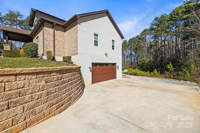 view of side of property with concrete driveway, brick siding, an attached garage, and stucco siding