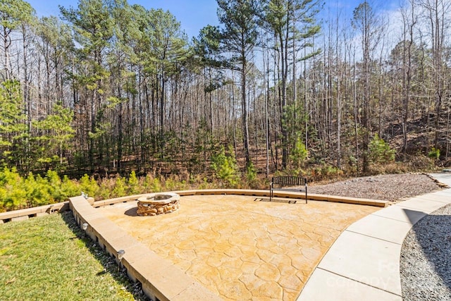 view of patio with an outdoor fire pit and a wooded view