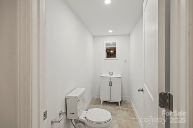 half bath featuring recessed lighting, baseboards, vanity, and toilet