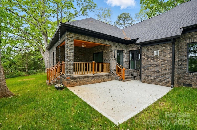 rear view of house with a lawn, brick siding, a patio area, and roof with shingles