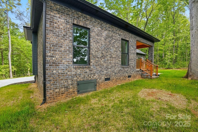 view of side of home featuring brick siding, a lawn, and crawl space