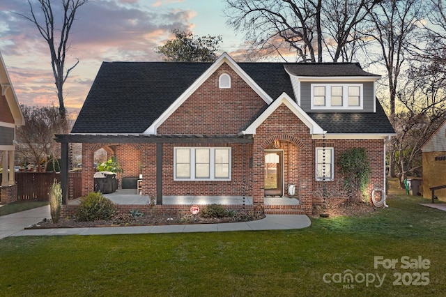 view of front of home featuring brick siding, roof with shingles, fence, a patio area, and a front yard