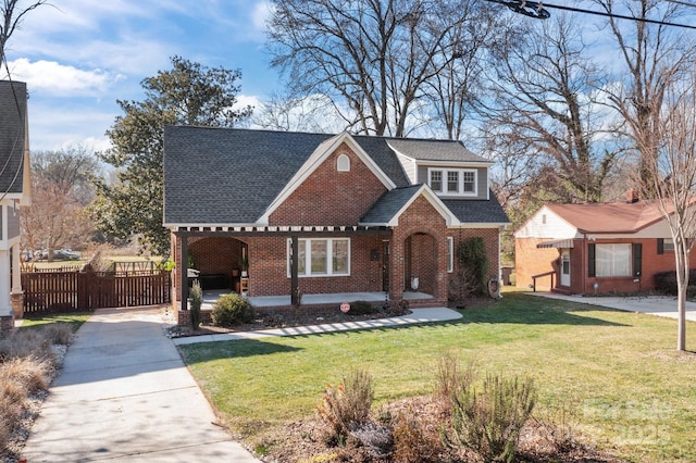 view of front facade featuring brick siding, a front lawn, a shingled roof, and fence