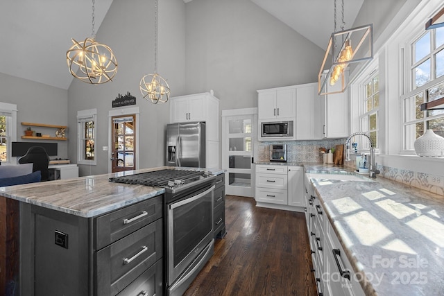 kitchen featuring light stone counters, a notable chandelier, stainless steel appliances, white cabinetry, and a wealth of natural light